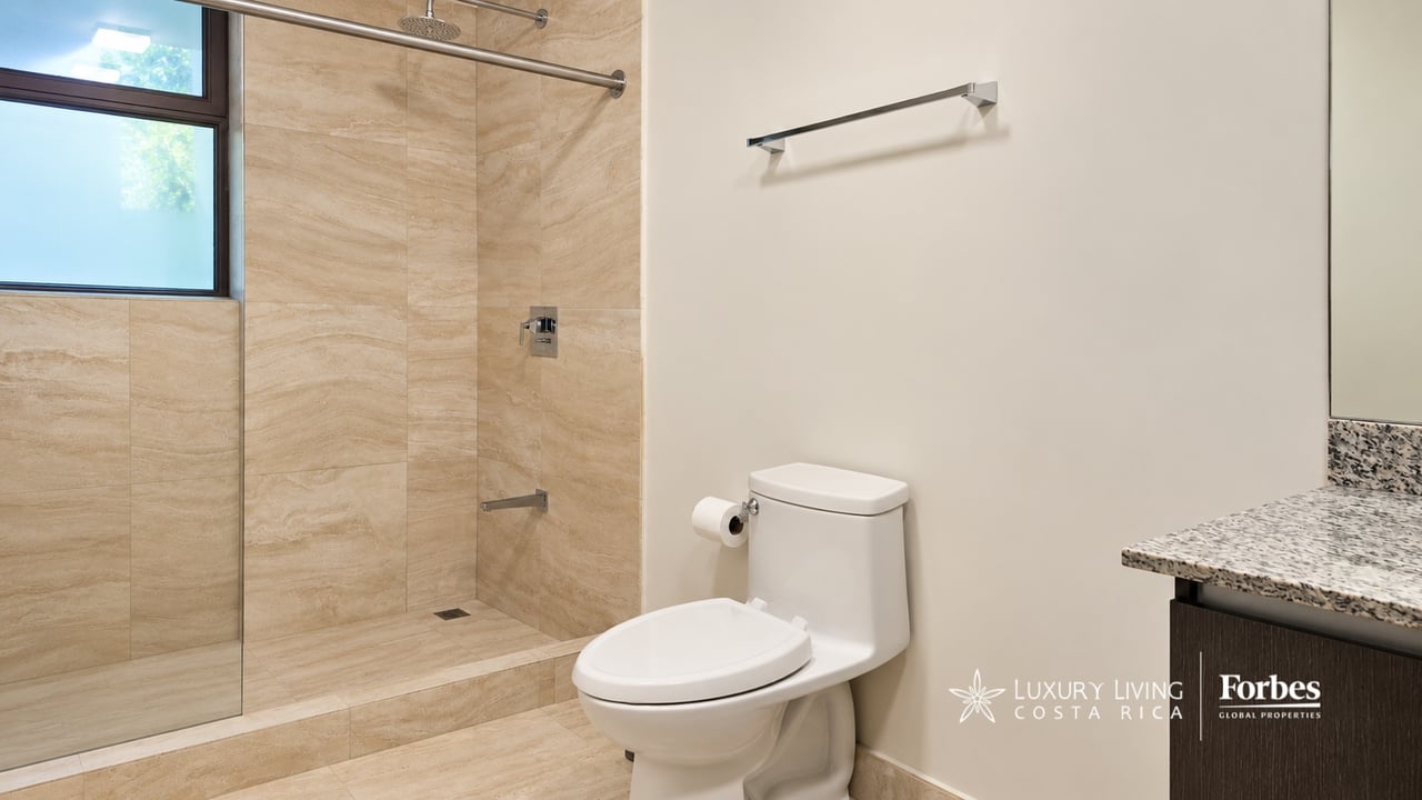 Modern bathroom with a beige stone-tiled walk-in shower, toilet, and granite vanity.