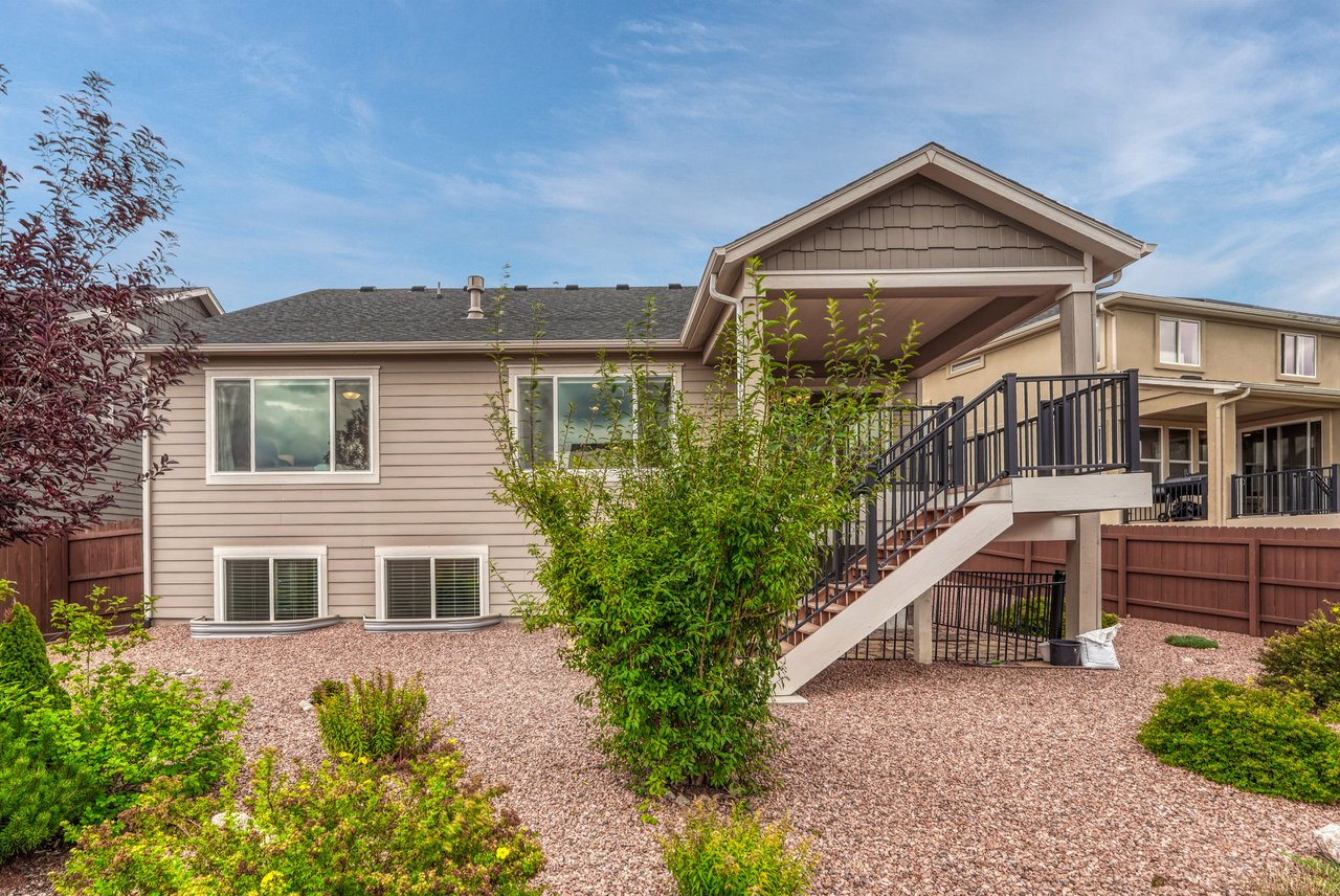 Back of the home with covered deck and stairs to the landscaped yard