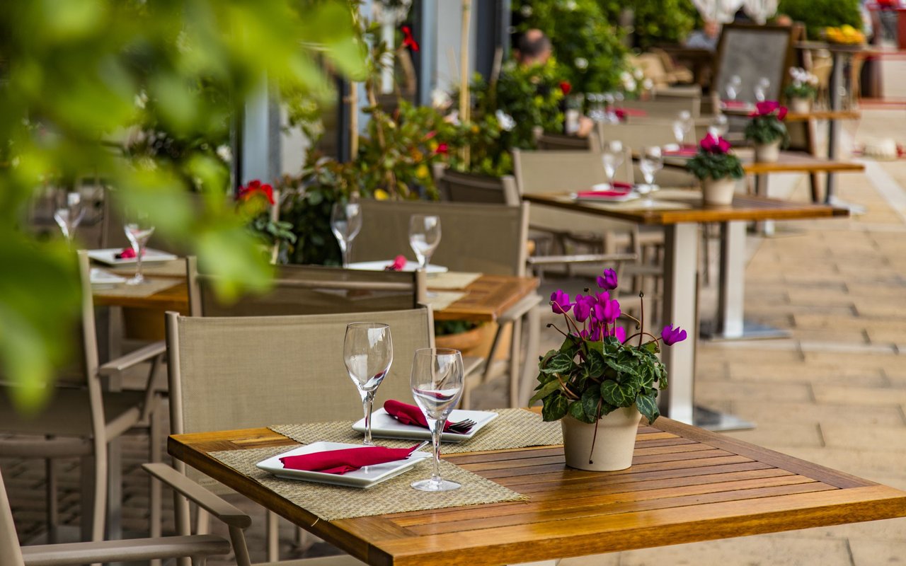 Outdoor restaurant patio with wooden tables, red napkins, wine glasses, and purple flowers.