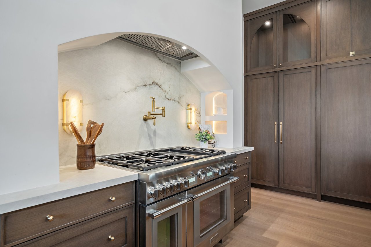 Luxury kitchen with a professional gas range, veined stone backsplash, brass fixtures, and dark wood cabinetry.
