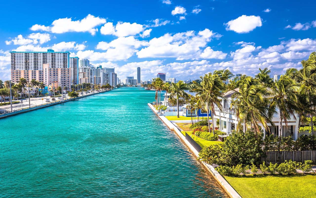 Turquoise waterway between high-rise buildings and palm-lined waterfront homes.