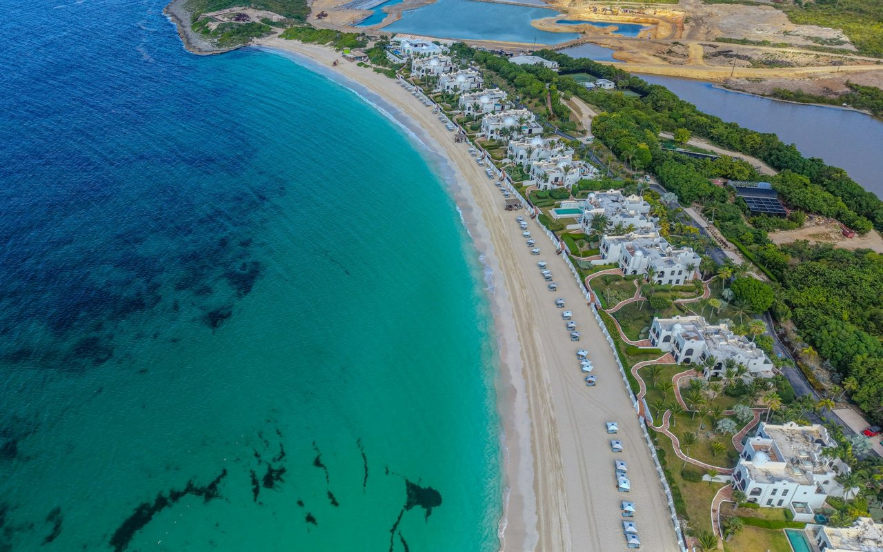 Aerial view of white coastal residences lining a sandy beach beside turquoise water.