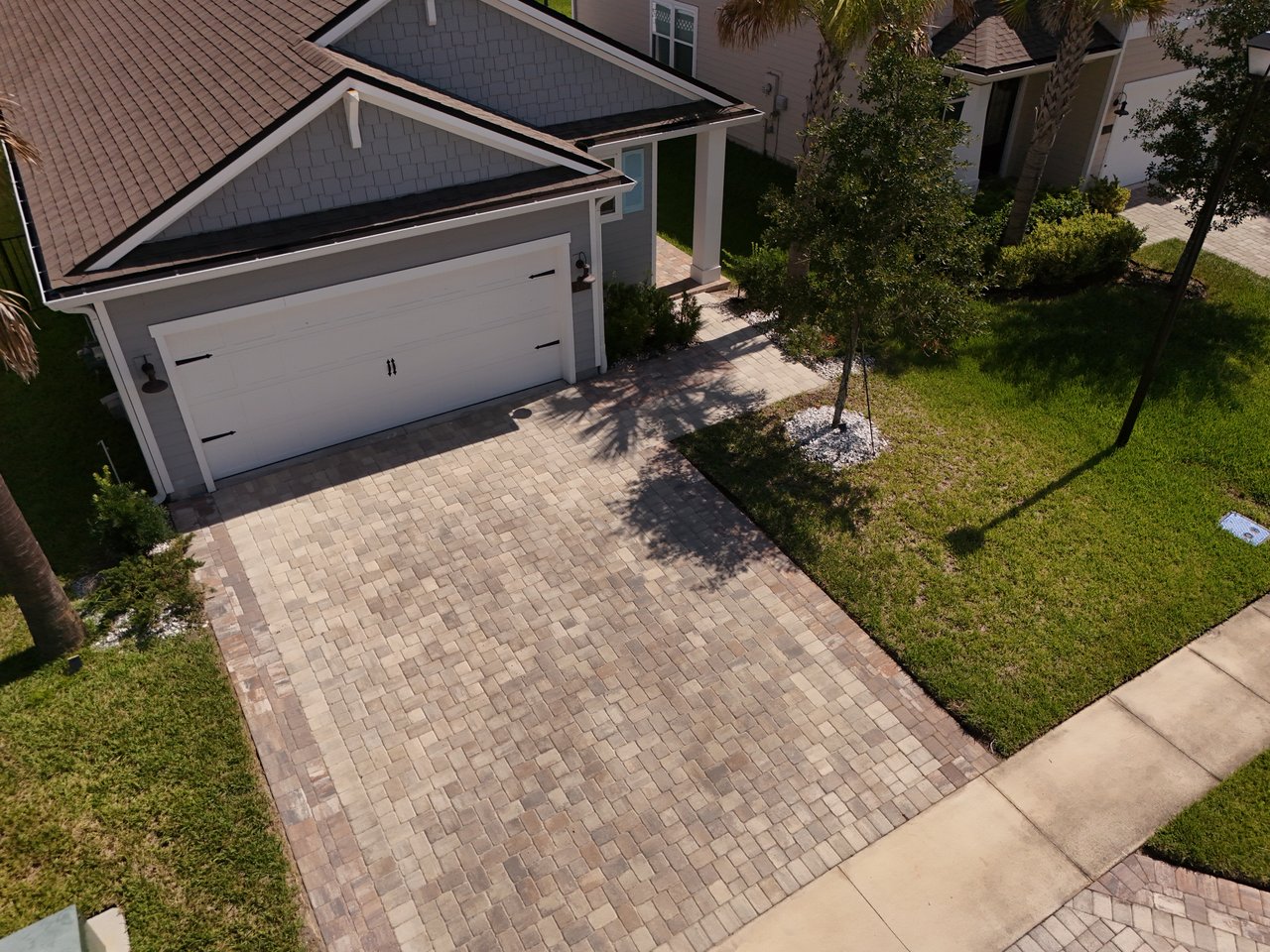 Aerial view of a gray home with a white double garage and broad paver driveway.