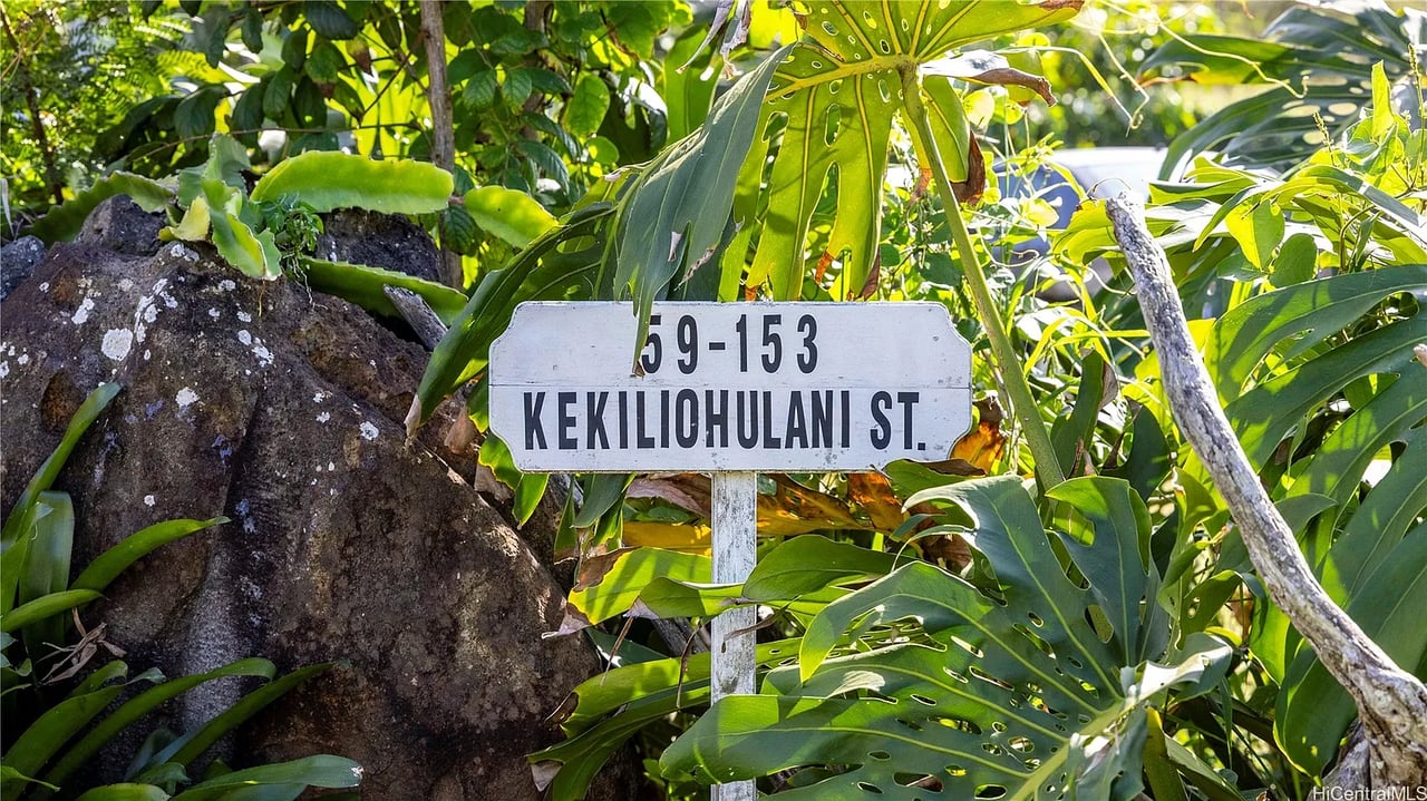 Kekiliohulani Street address sign surrounded by tropical foliage and volcanic rocks.