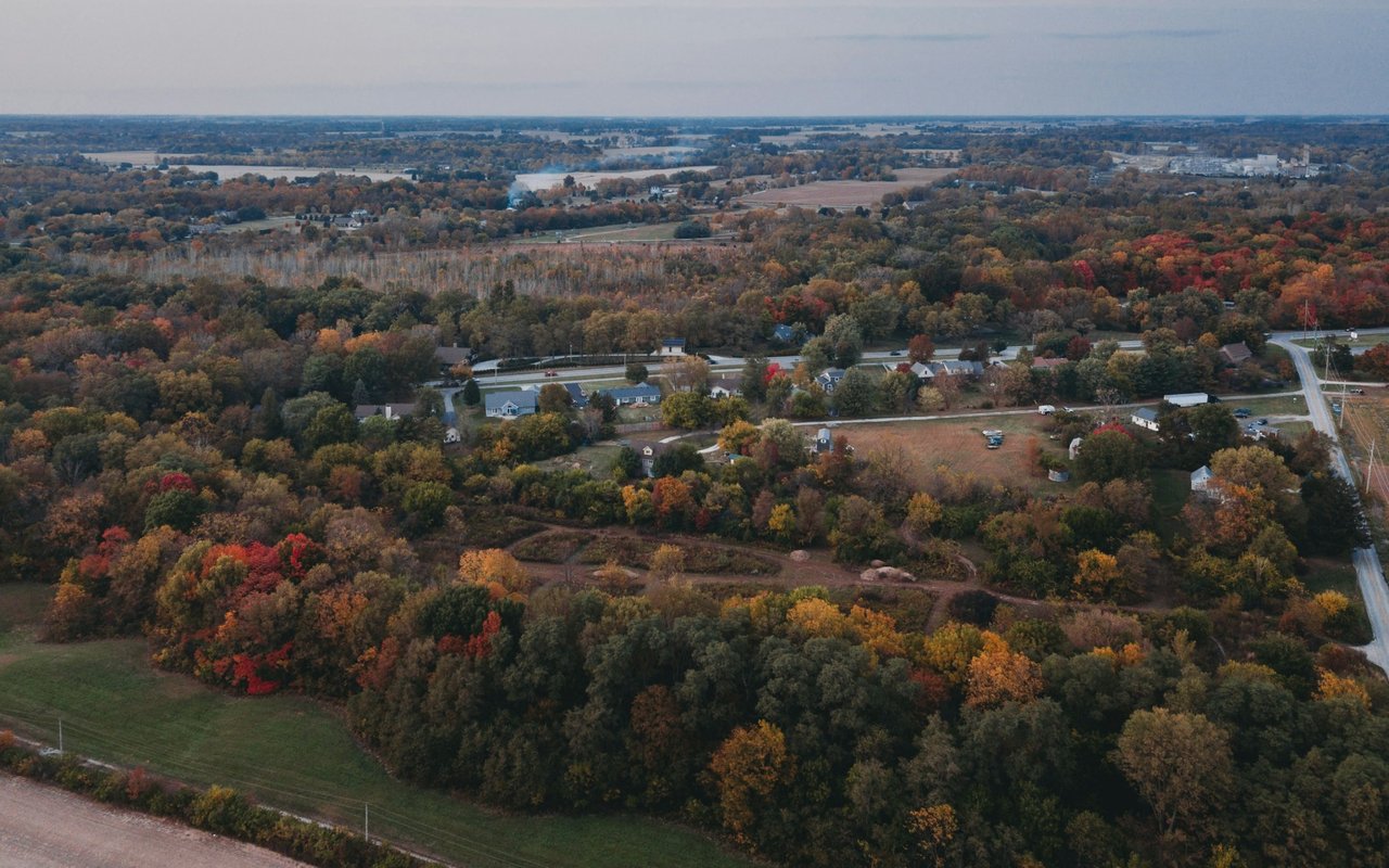 Aerial view of homes and roads among autumn-colored trees and open fields.