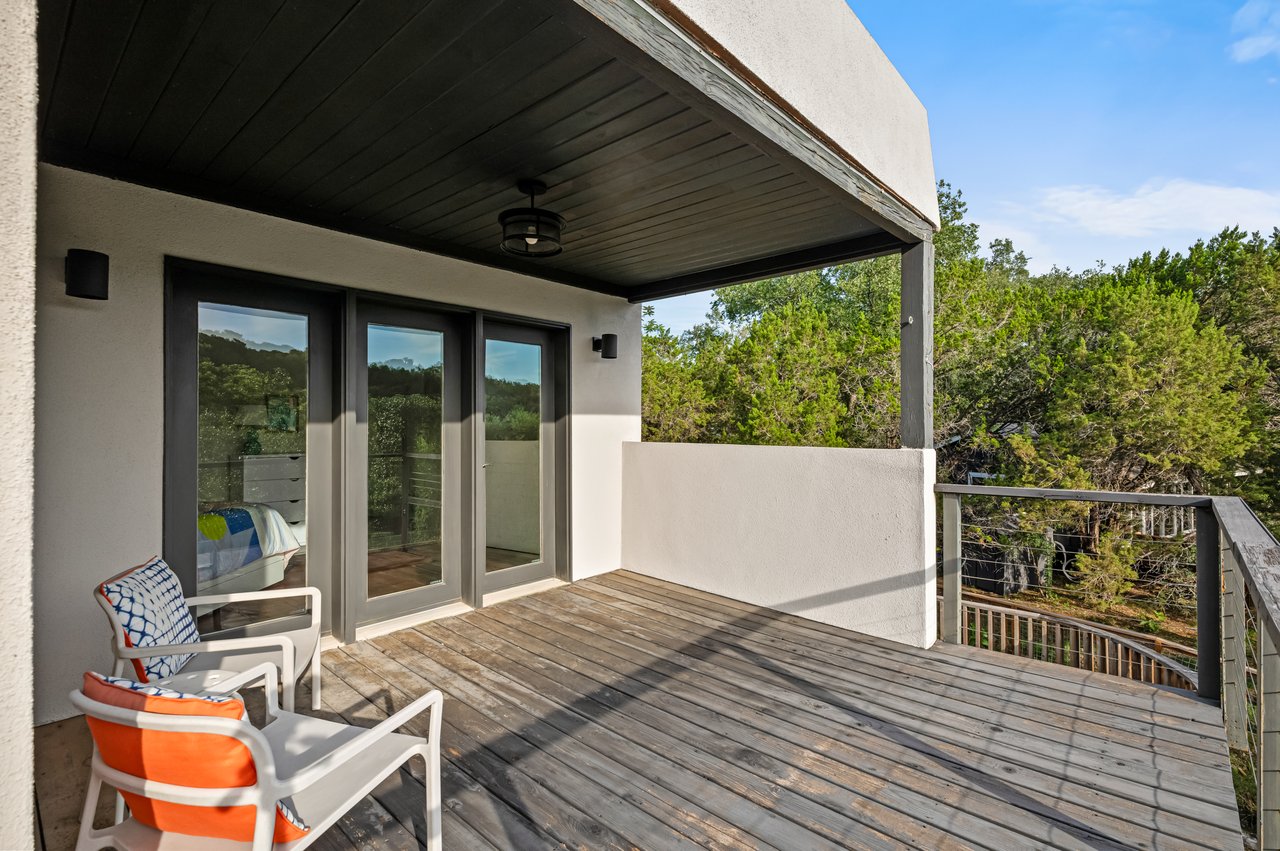 Covered wooden deck with colorful cushioned chairs and a view of trees.
