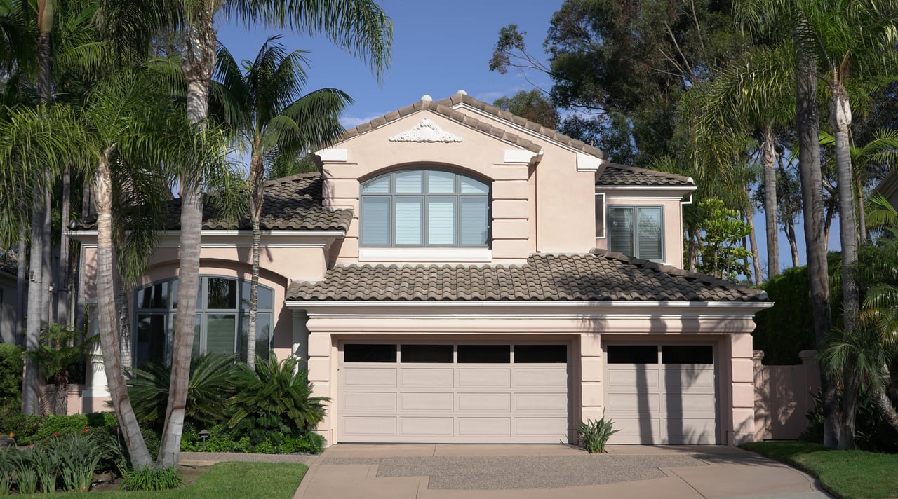 Two-story stucco home with a tiled roof and three-car garage, framed by tall palm trees.