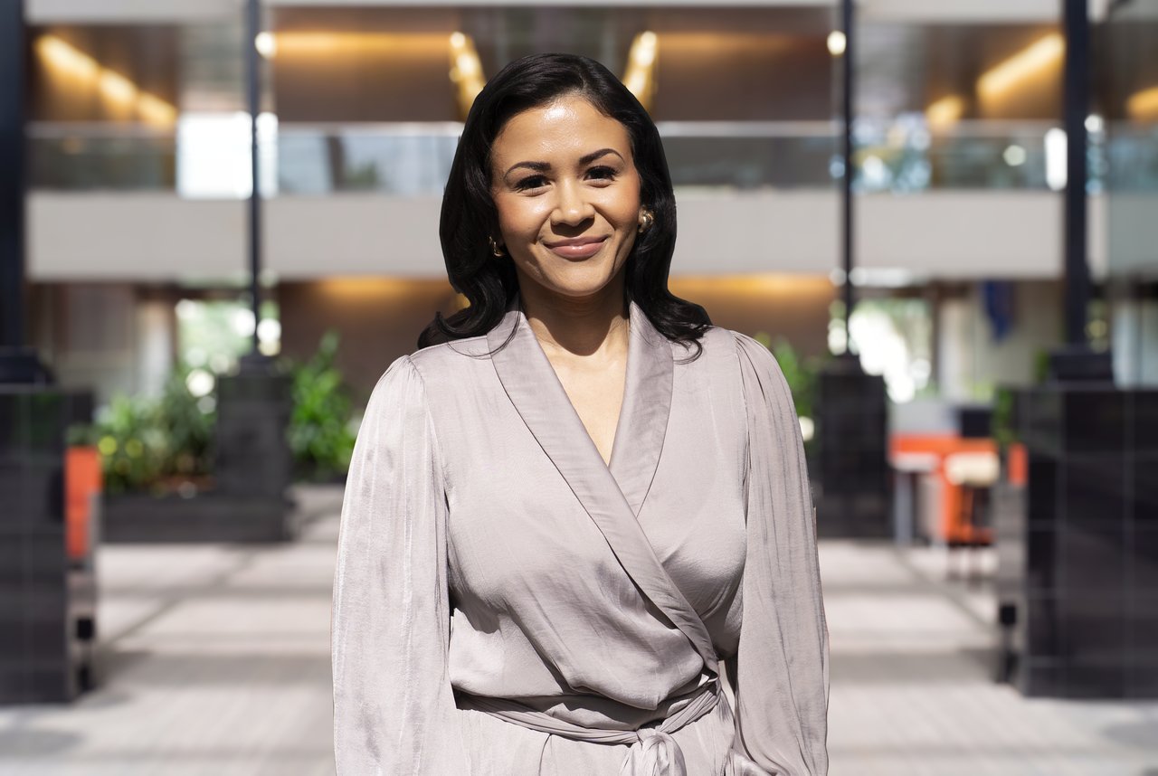 Naomy Valeriano smiles in a light wrap blouse in a modern office atrium.