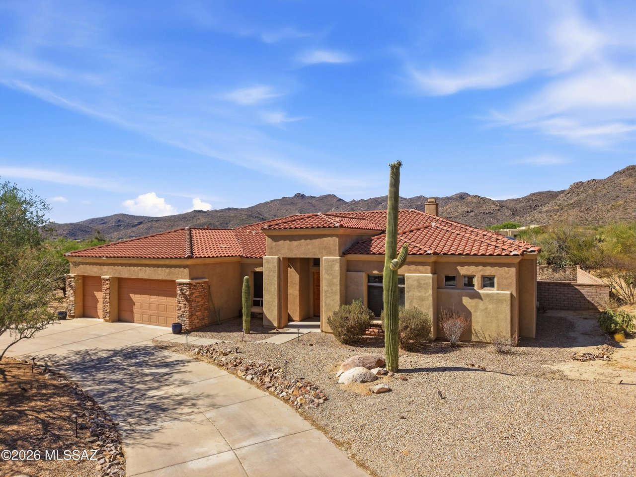 Desert home with a red tile roof, saguaro cacti, and mountains in the background.