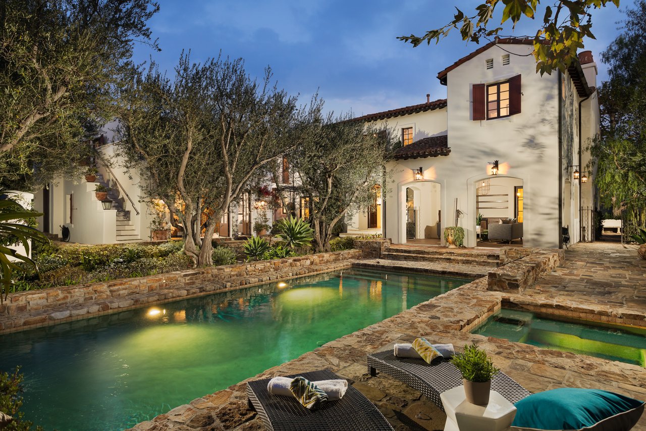 White stucco home with red tile roofs and a stone-edged swimming pool at dusk.