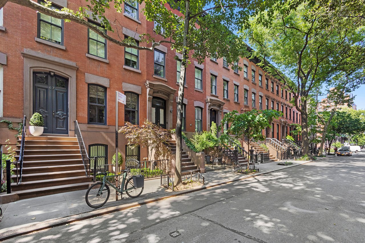 Red-brick townhouses with front stoops and leafy trees line a sunny street.