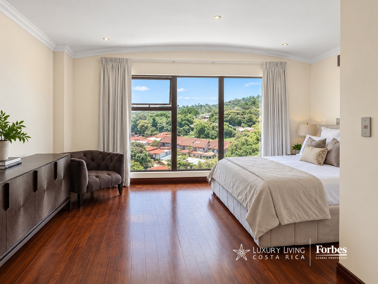 Penthouse bedroom with a large bed and floor-to-ceiling windows overlooking a green hillside.