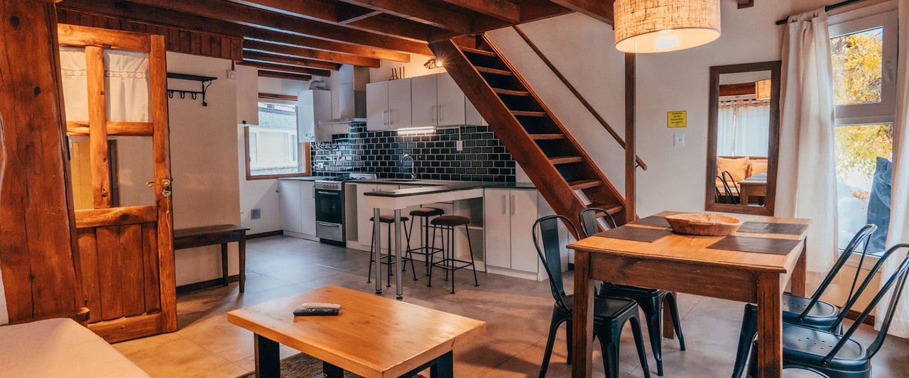 Open-plan kitchen and dining area with a timber staircase, dark ceiling beams and black tile backsplash.