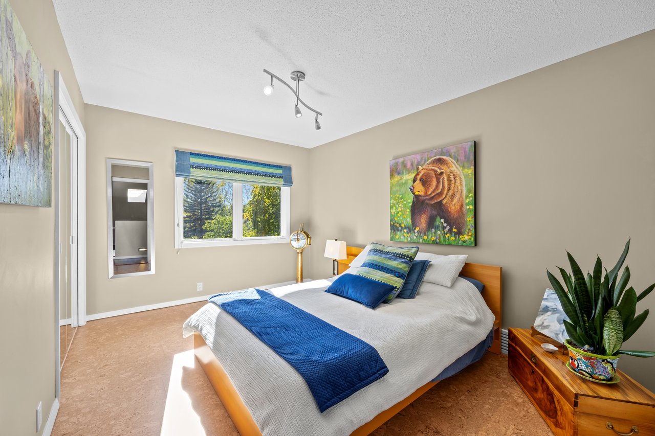 Bedroom with blue and white bedding, leafy views through the window, and a colorful bear painting.