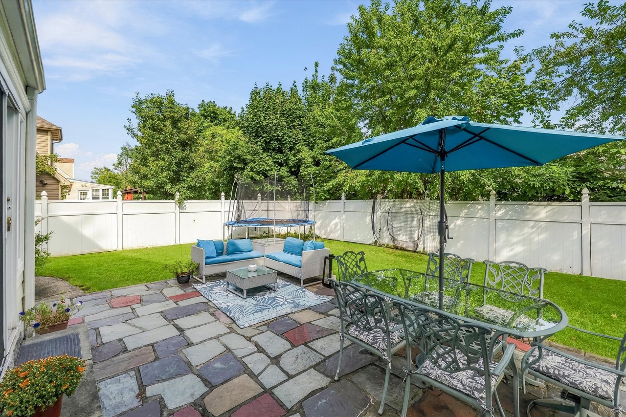 Fenced backyard with a slate patio, outdoor dining set under a blue umbrella, and lounge seating.