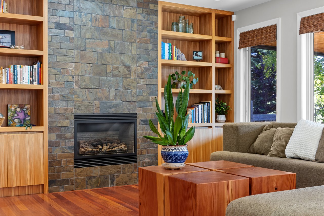 Living room with a stone fireplace, built-in wood bookshelves, and a sofa beside the windows.