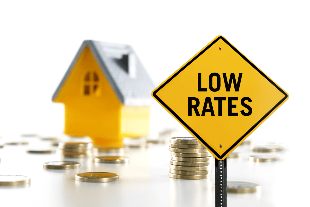 low rates sign in front of a toy house and piles of coins