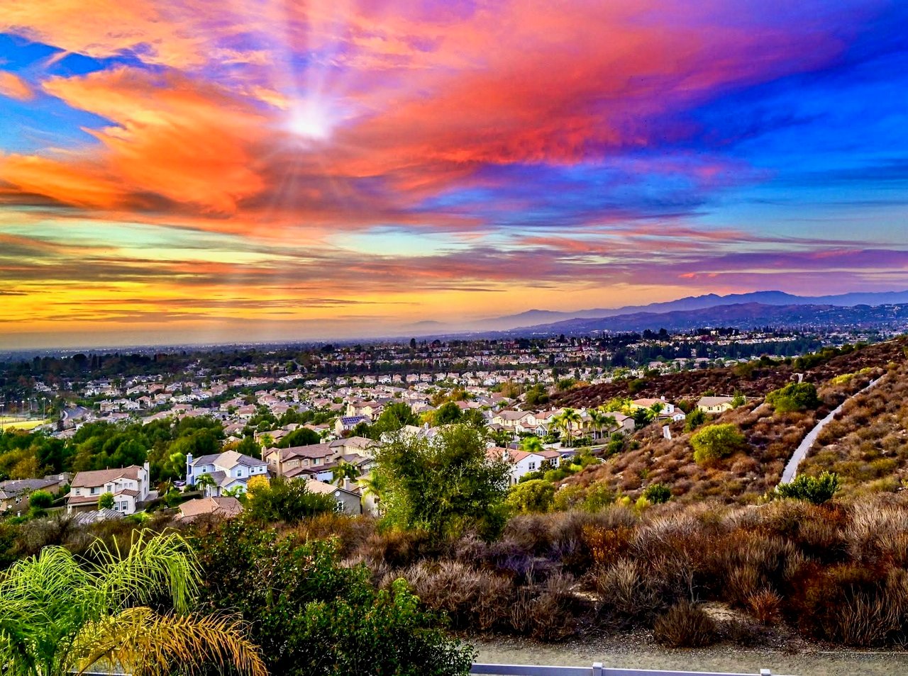 Suburban neighborhood and distant mountains beneath vivid sunset clouds.