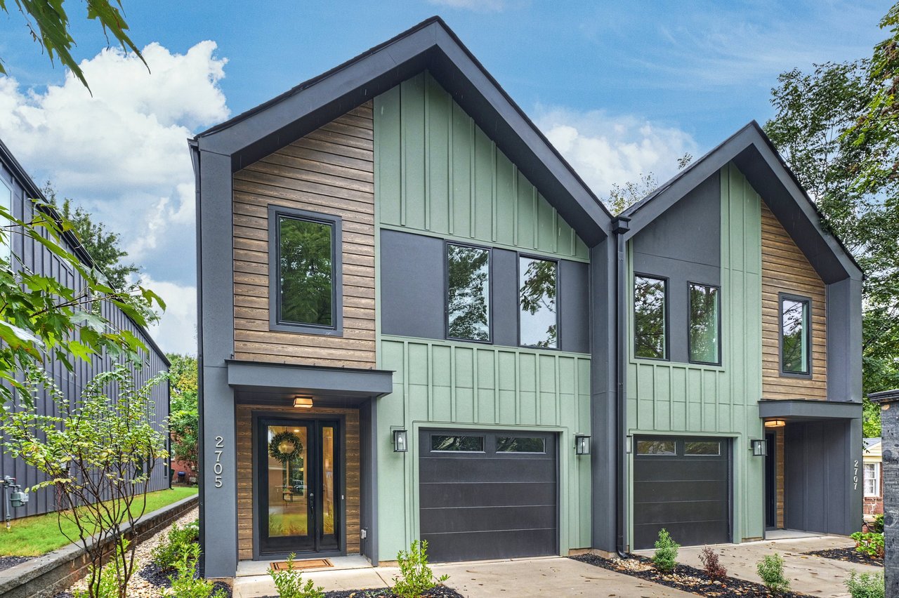 Modern attached home with angular gables, sage-green siding, wood accents, and a dark garage door.