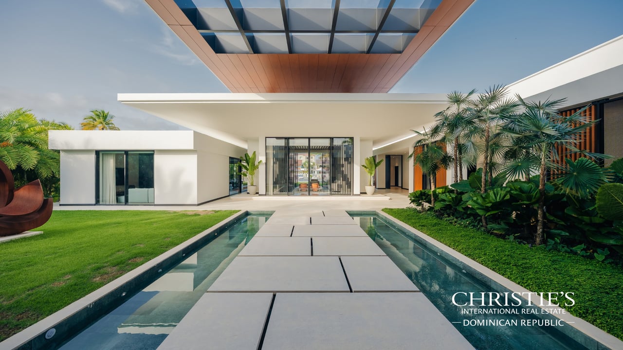 Modern villa courtyard with a reflecting pool, broad stepping-stone path, and tropical landscaping.
