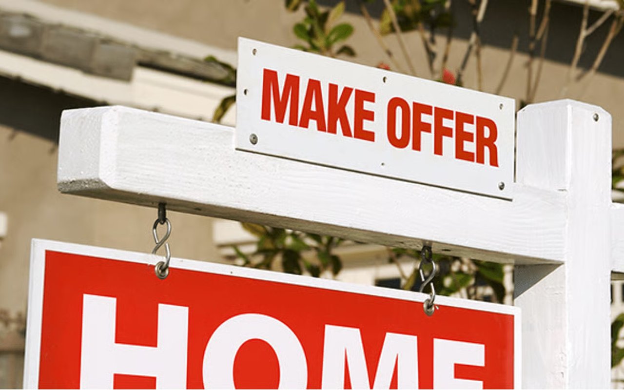 Real estate sign with a “MAKE OFFER” placard above a red home sign.