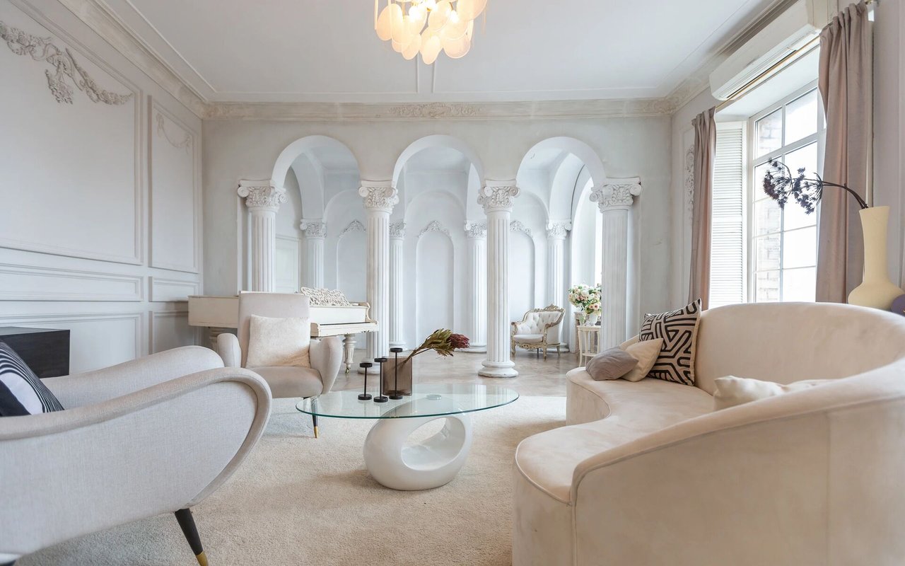 Elegant living room with ornate white arches, a piano, and pale curved sofas.