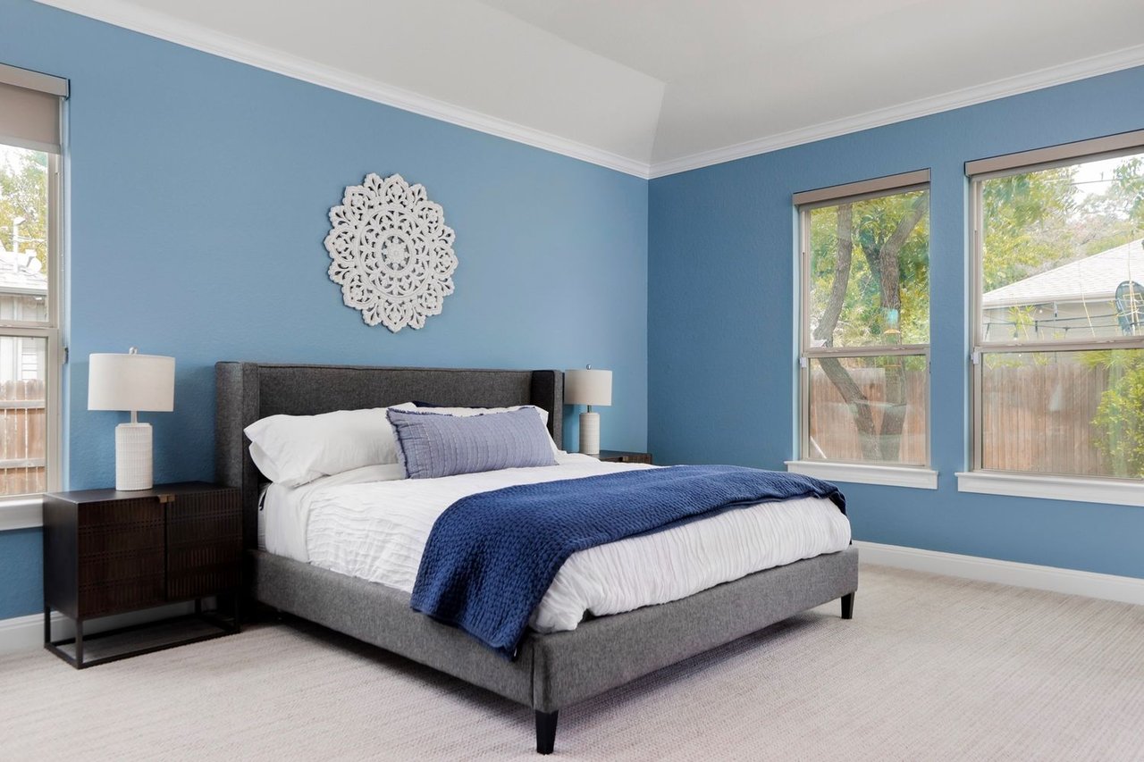 Staged bedroom with blue walls, a gray bed, navy throw, and large windows.
