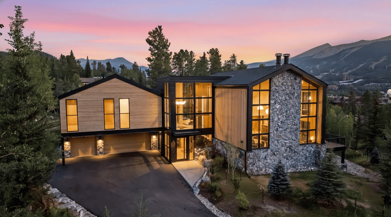 Modern mountain home with timber siding, a stone facade, and glowing windows at dusk.
