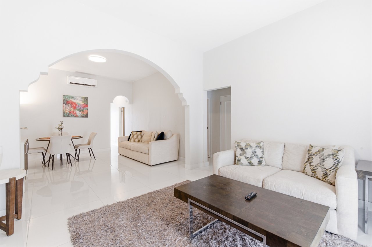 Furnished living and dining room with white sofas and a broad arched opening.