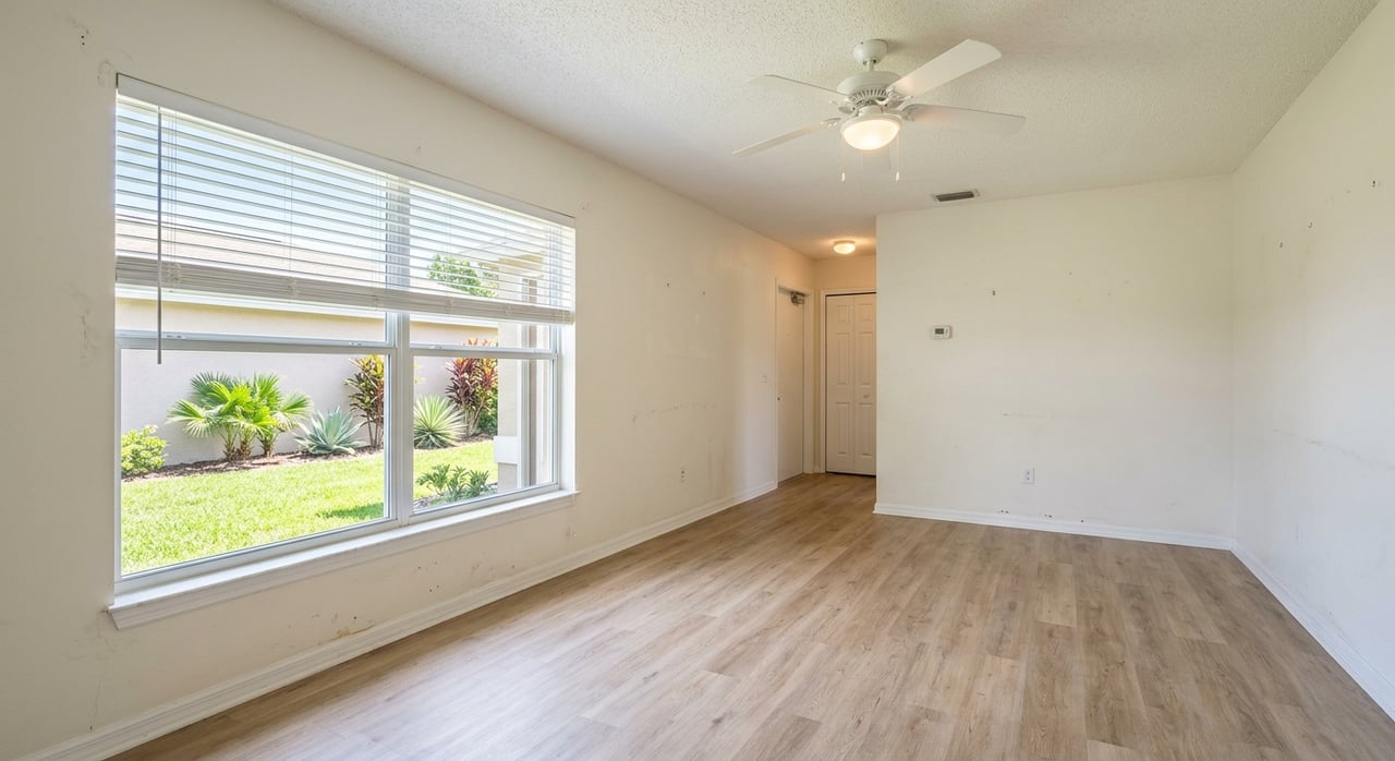 Empty living room with closed blinds, honey-oak flooring, and a ceiling fan above.