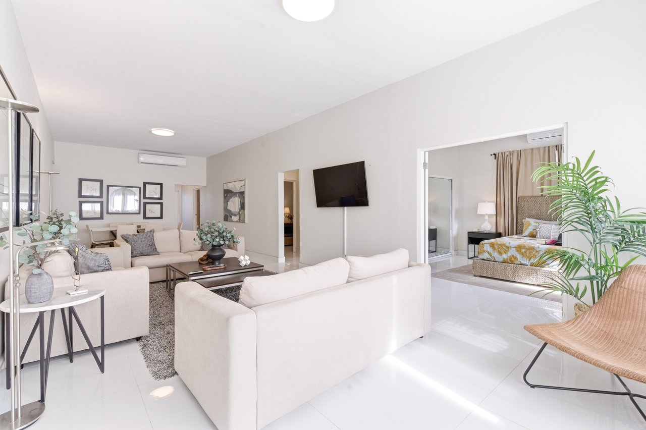Furnished living room with white sofas, glossy tile floors, and an adjoining bedroom.