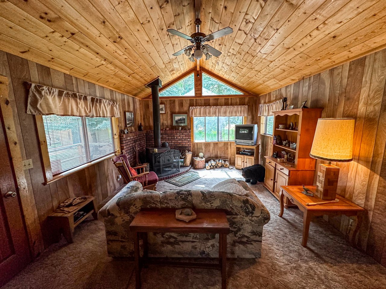 Rustic living room with vaulted wood ceiling, brick fireplace, and large windows.