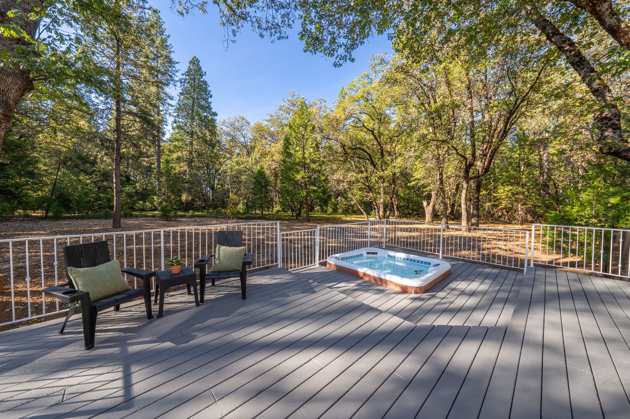 Wooded deck with a hot tub, outdoor chairs, and autumn trees.