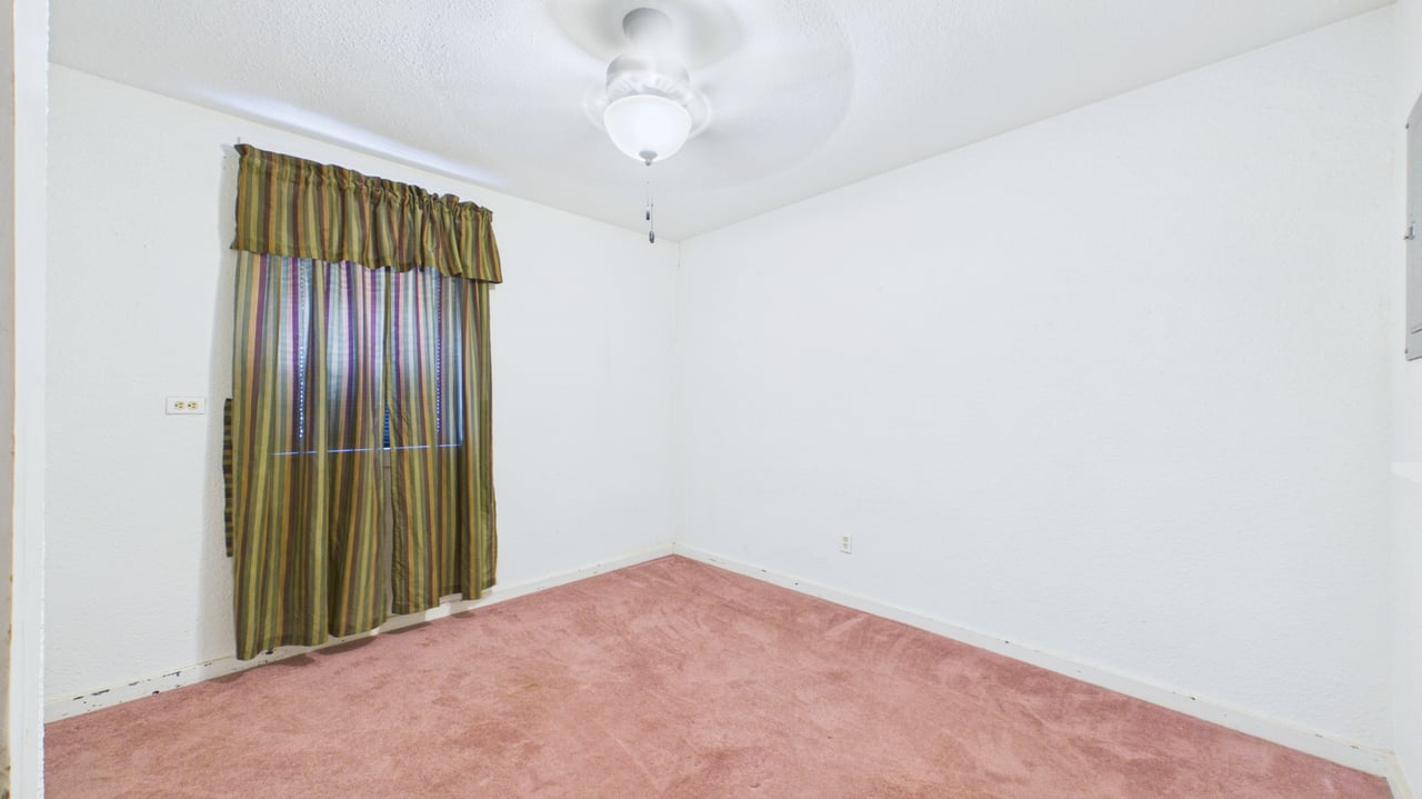 Empty room with pink carpet, striped curtains, and a ceiling fan with light.