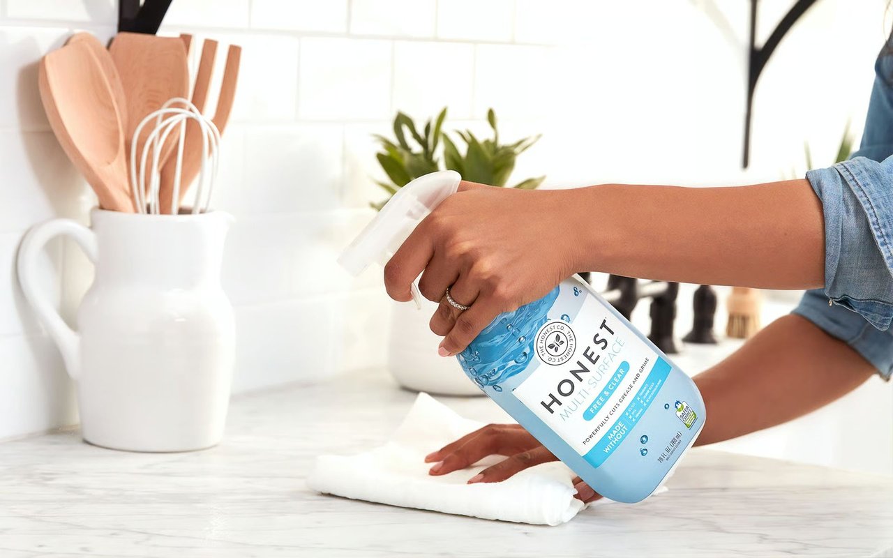 A person sprays cleaner on a kitchen counter while wiping it with a white cloth.