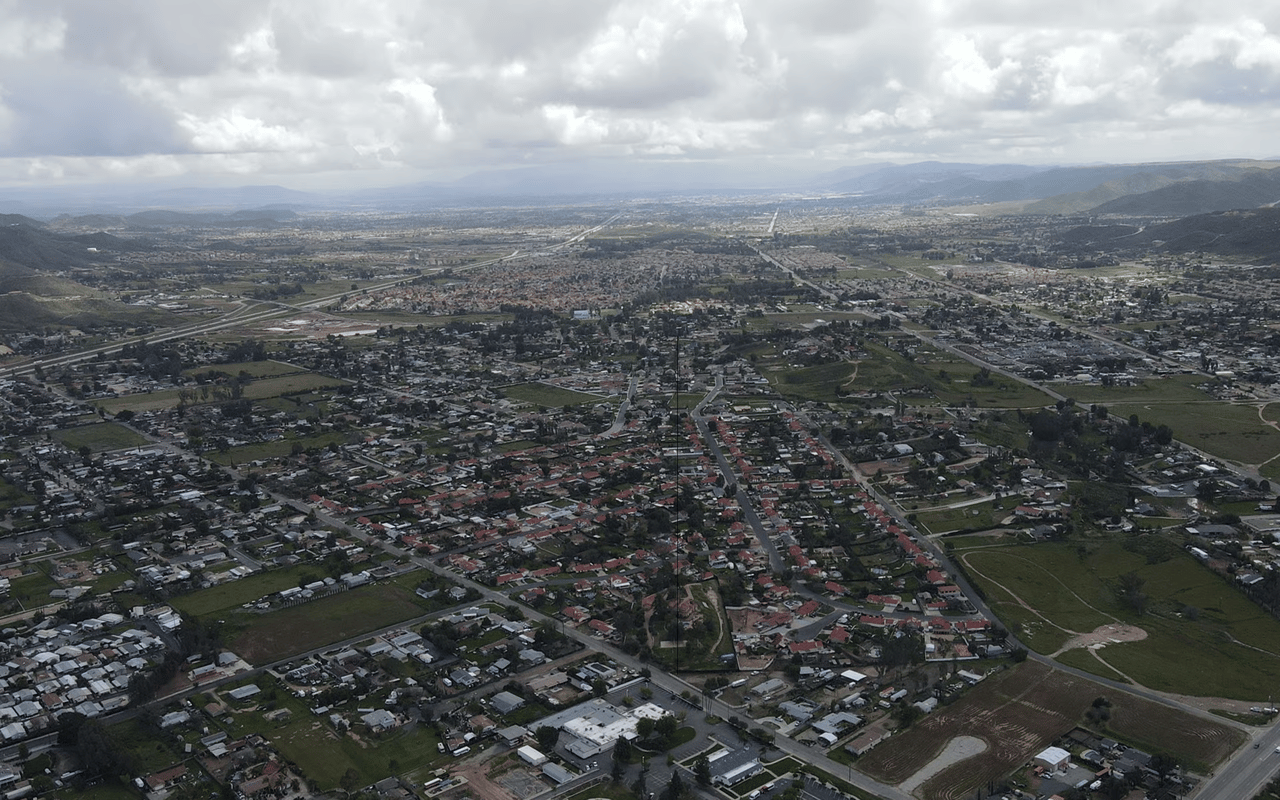 Aerial view of a sprawling neighborhood with open fields and distant rolling hills.