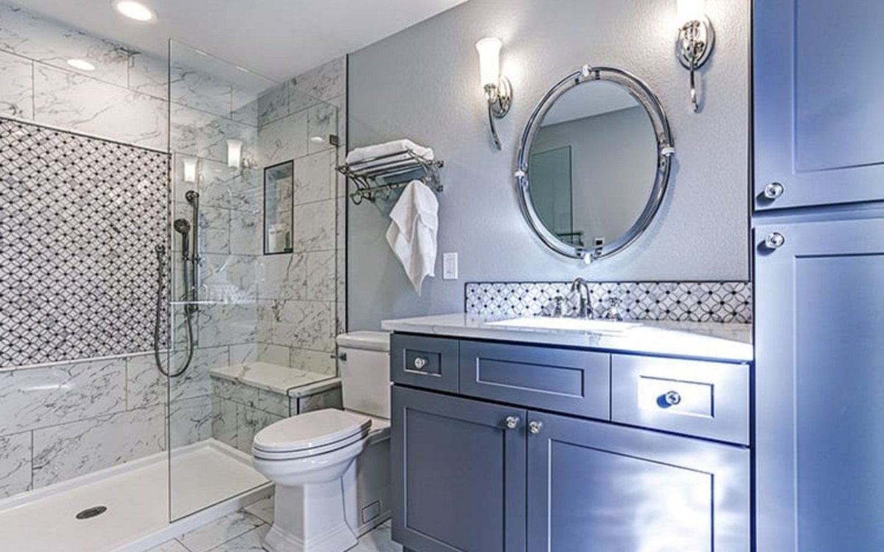 Bathroom with a glass walk-in shower, marble-look tile, and blue vanity with round mirror.