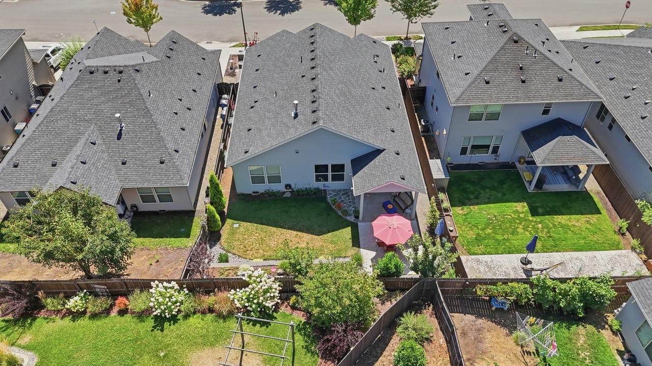 Aerial view of suburban homes and fenced backyards with lawns, patios, and outdoor furniture.