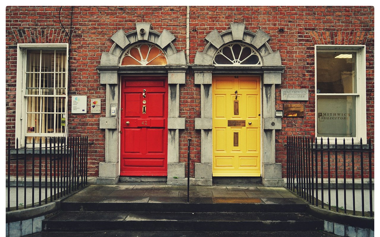 Brick building facade with ornate red and yellow doors and iron railings.