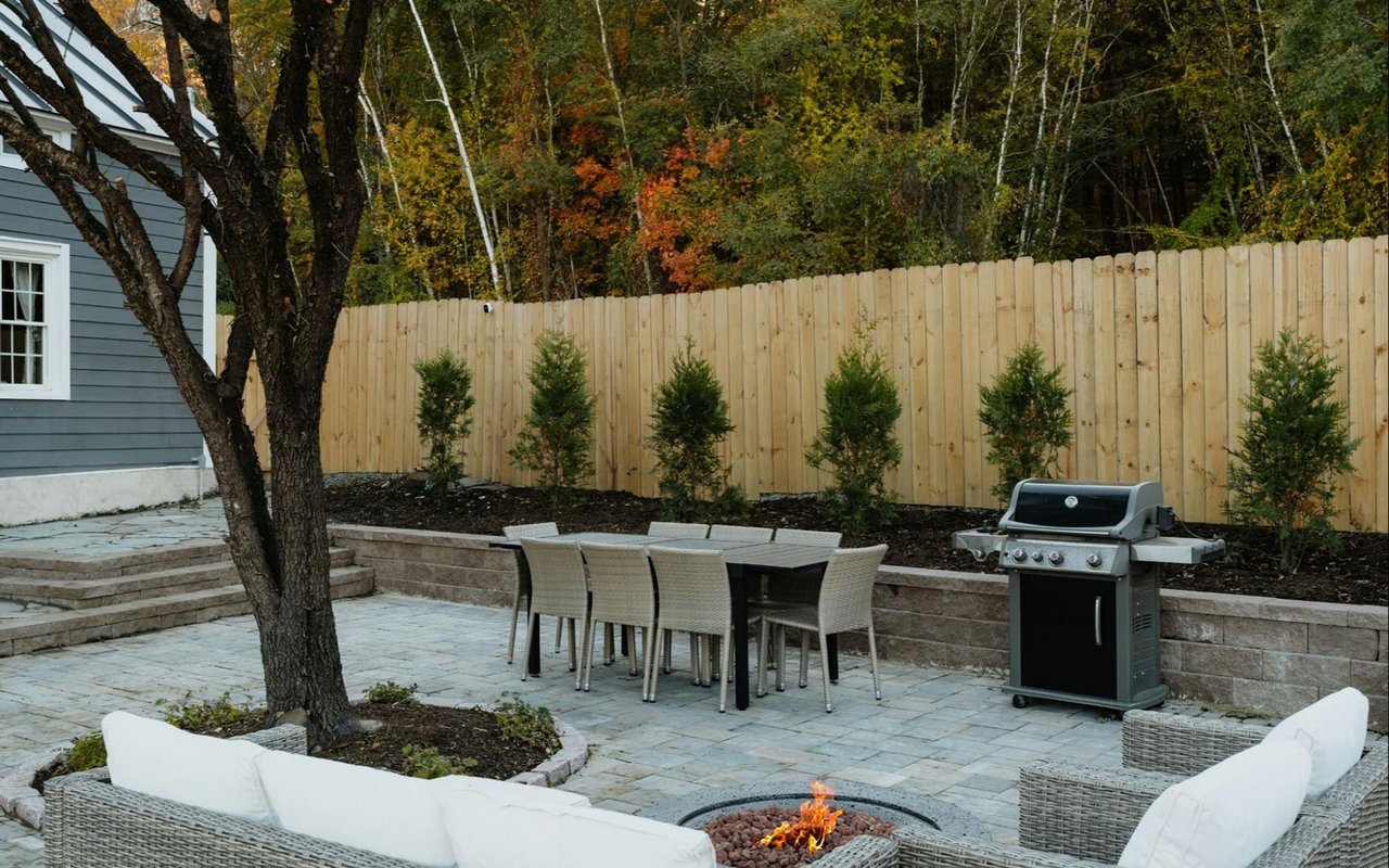 Backyard patio with wicker seating around a fire pit, dining table, and barbecue grill.
