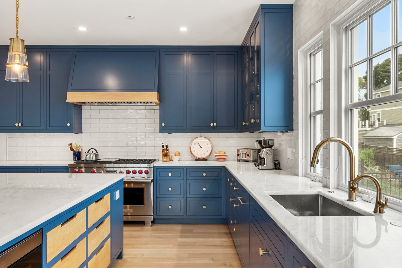 Kitchen with navy cabinetry, white stone counters, stainless range, and large windows above the sink.