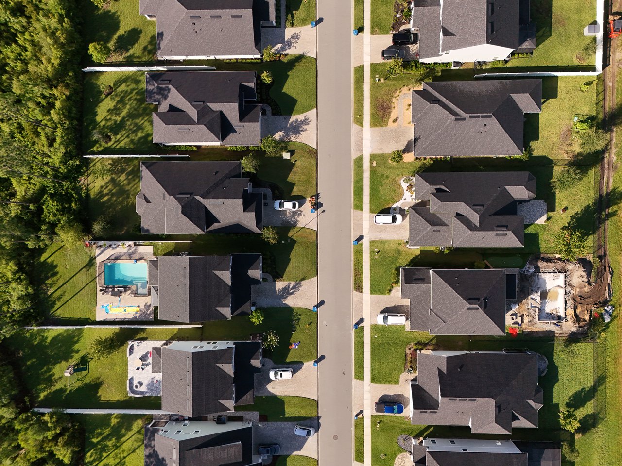 Aerial view of homes along a residential street, including a backyard pool and tree-lined yards.