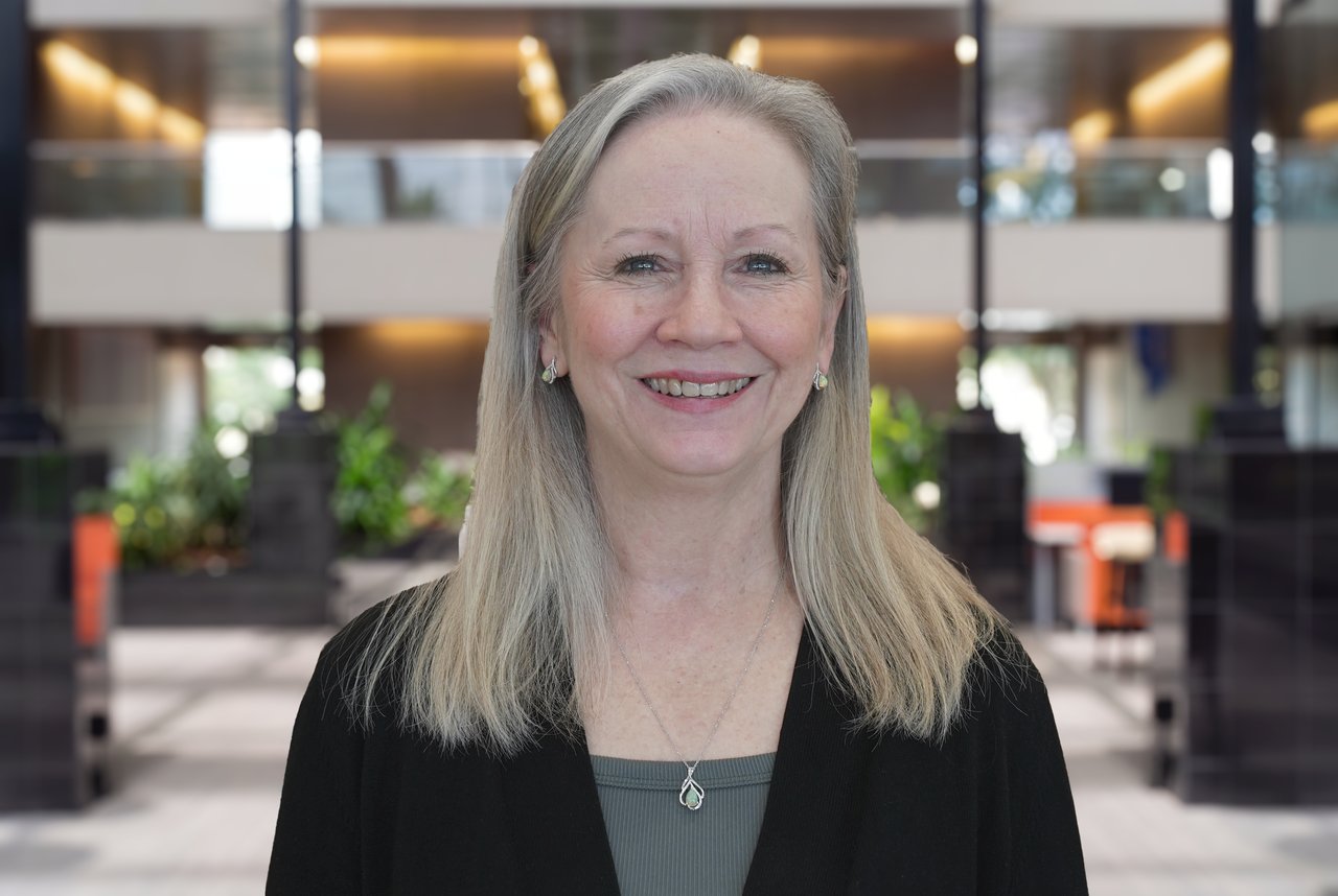 Beth Klein smiling in a black cardigan and gray top in a modern office lobby.