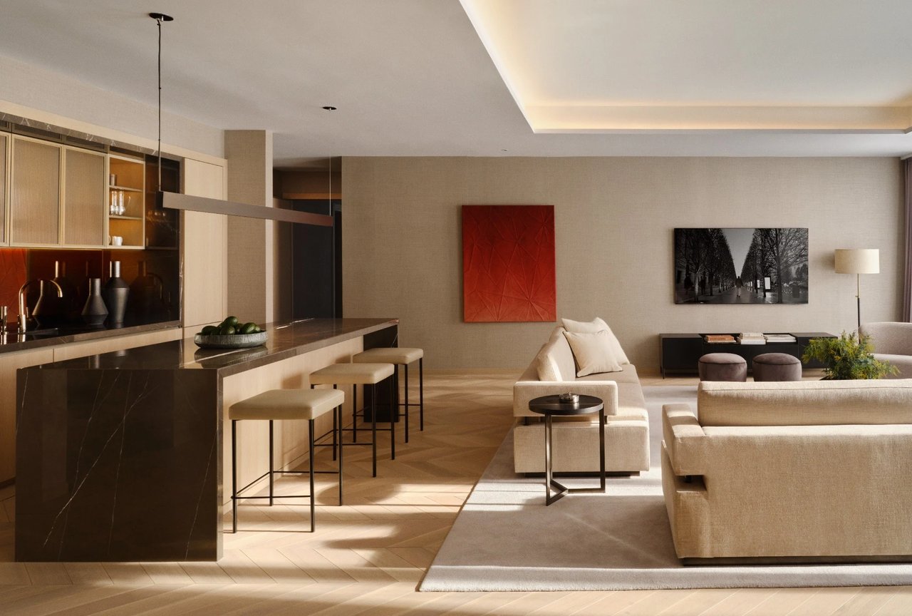 Luxury apartment living room and kitchen with a dark stone island, cream sofas, and warm wood floors.