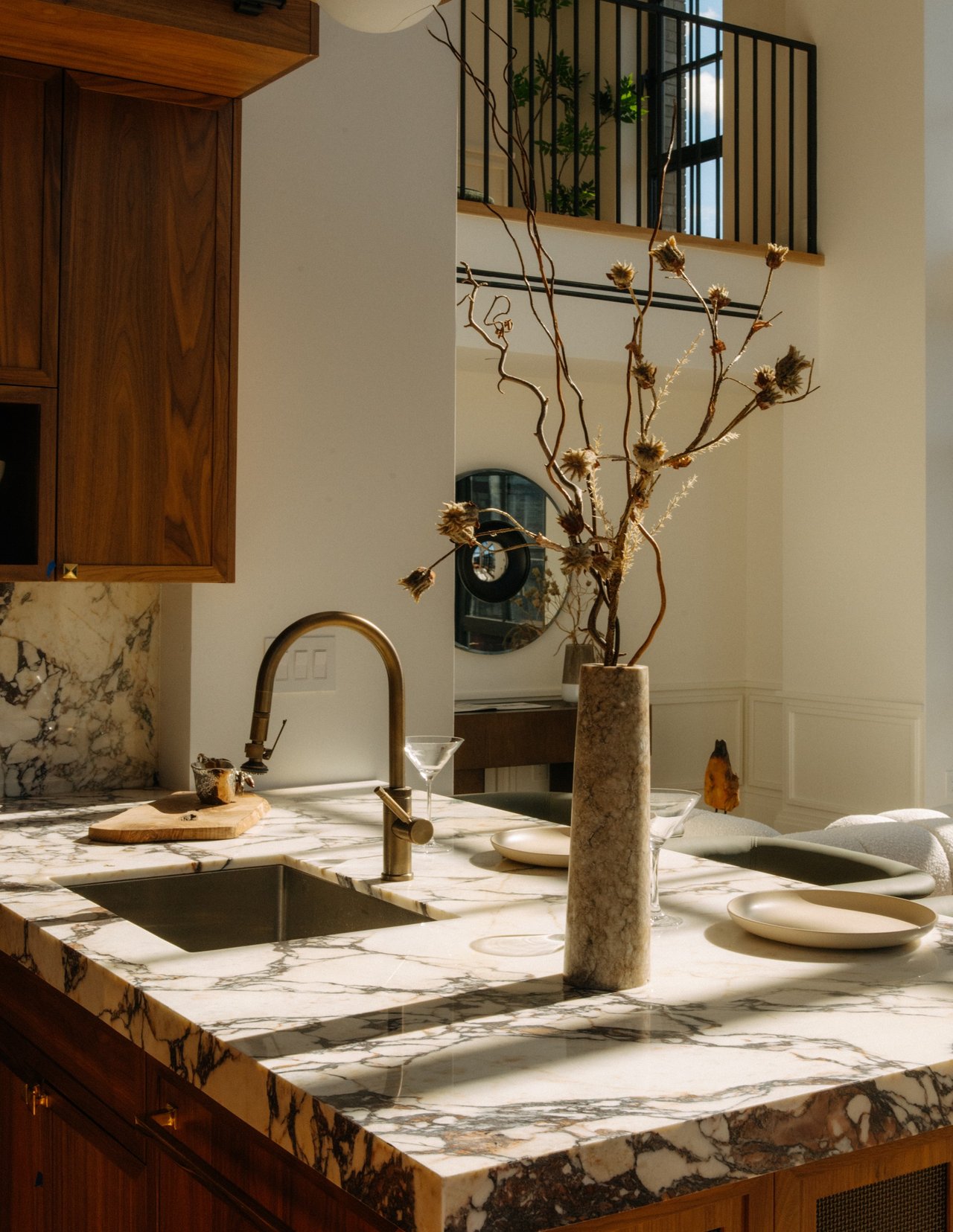 Kitchen with a veined marble island, brass faucet, dark wood cabinetry, and dried branches.