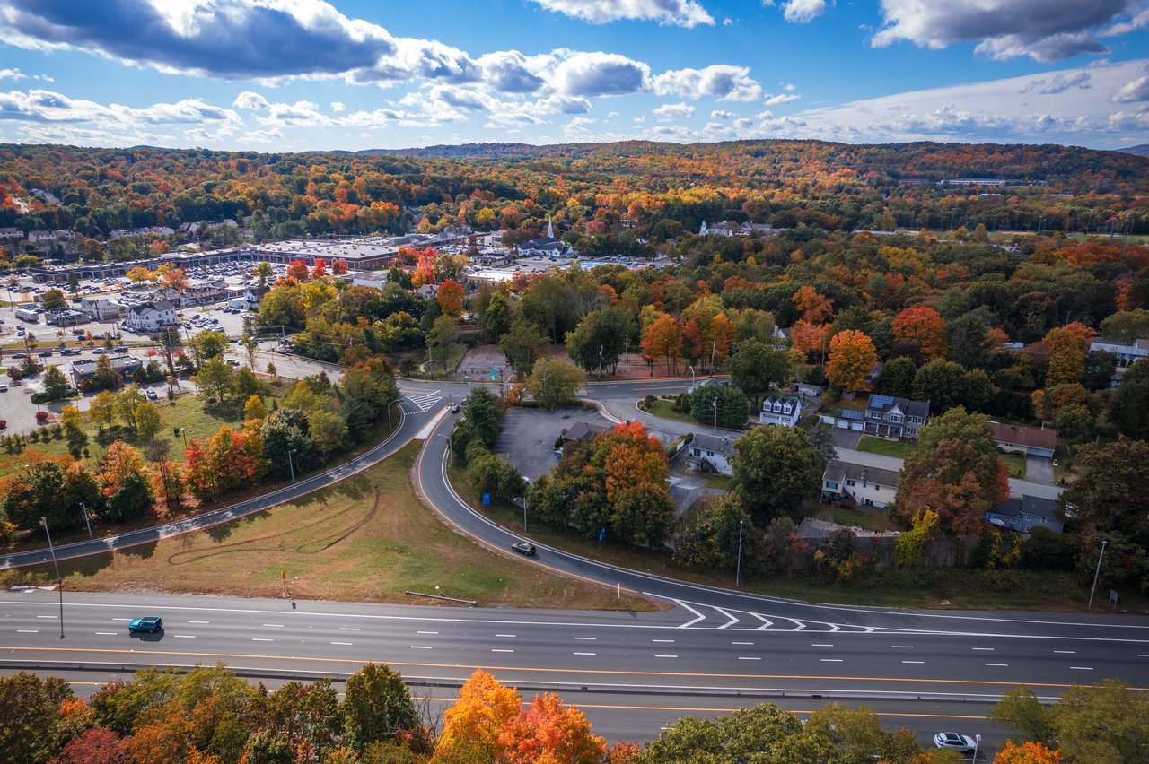 Aerial view of a suburban town surrounded by autumn foliage, with a divided highway in the foreground.