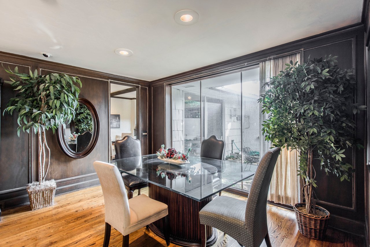 Dining room with a glass-top table, dark wood paneling, hardwood floors, and potted plants.