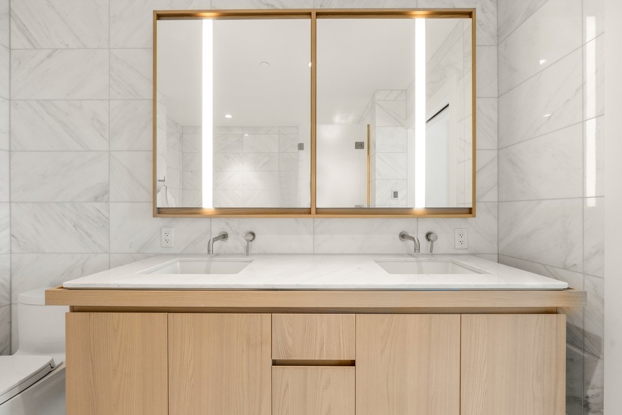 Bathroom with a double-sink wood vanity, wide mirror, and marble-patterned tile.