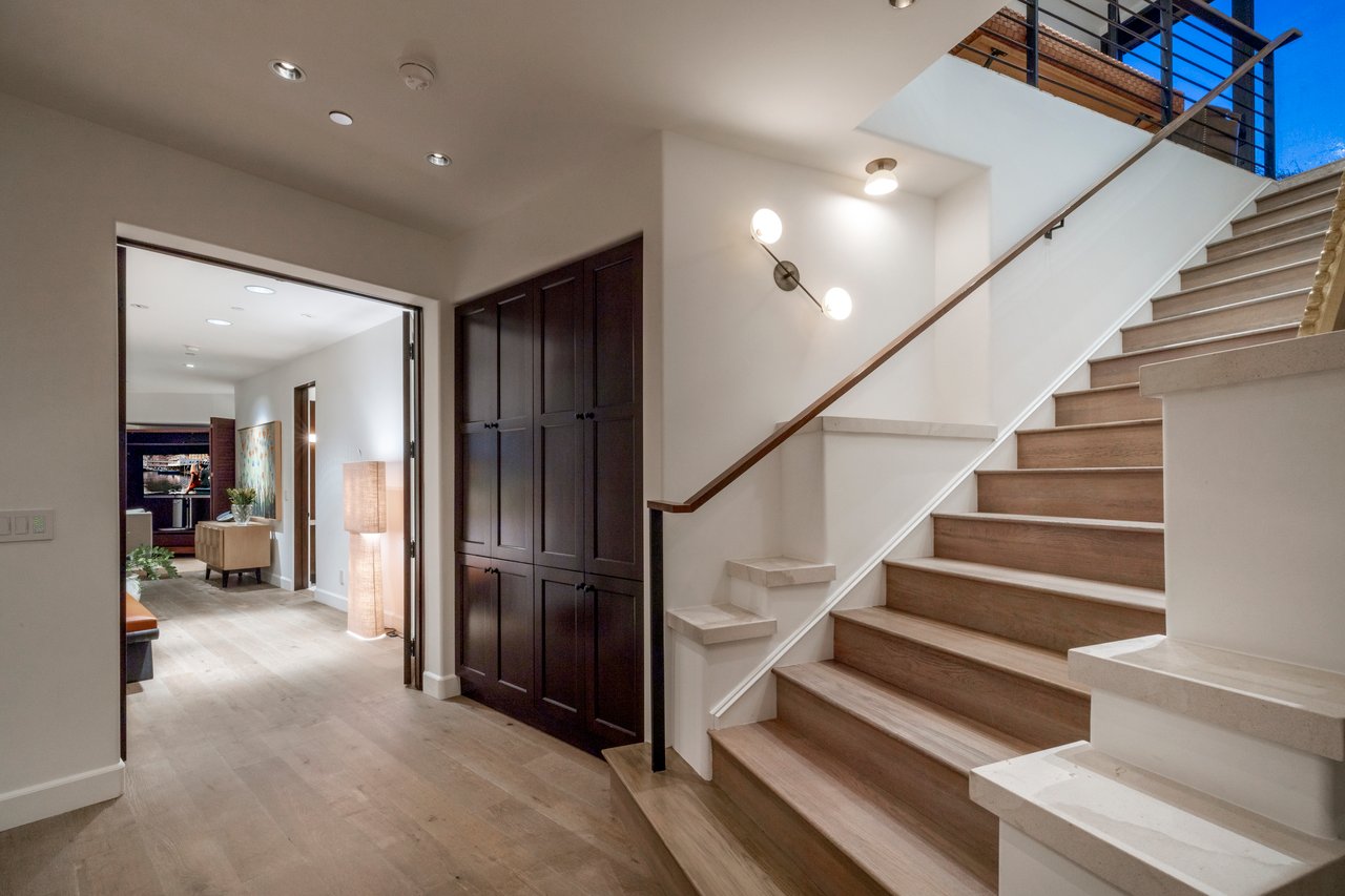 Home foyer with a broad wood staircase and dark built-in cabinets beside an open living area.
