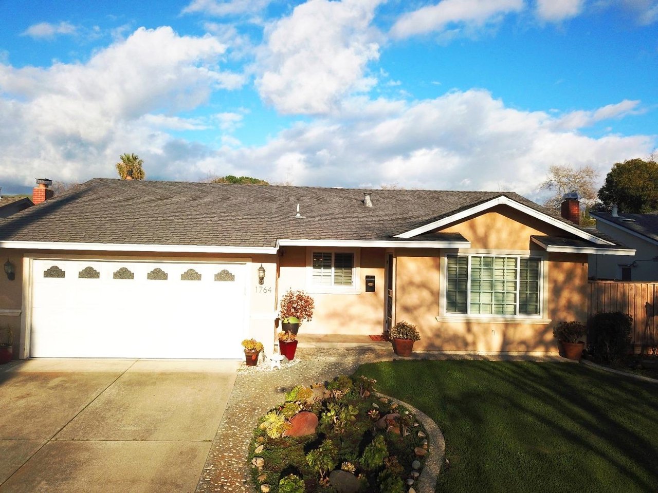 Single-story tan home with a double garage, curved garden bed, and front lawn.